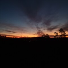 Serene landscape at sunrise, showcasing a vivid gradient of deep blue, purple, and fiery orange hues, with silhouetted trees against the glowing horizon. A tranquil morning scene.