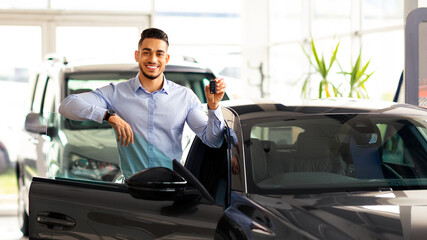 Wealthy middle eastern businessman buying new car in luxury auto showroom, cheerful arab guy...