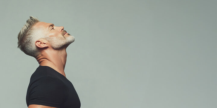 Fabulous at any age. Profile portrait of charismatic muscular 50 years old man standing over light gray background and smiling. Perfect haircut and body. Close-up. Copy-space. Studio shot