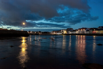 Fototapeta premium Low-angle night shot from the River Corrib, showcasing The Long Walk and Claddagh in Galway