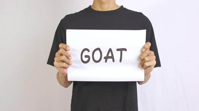 a footage of a man standing holding a paper that says GOAT