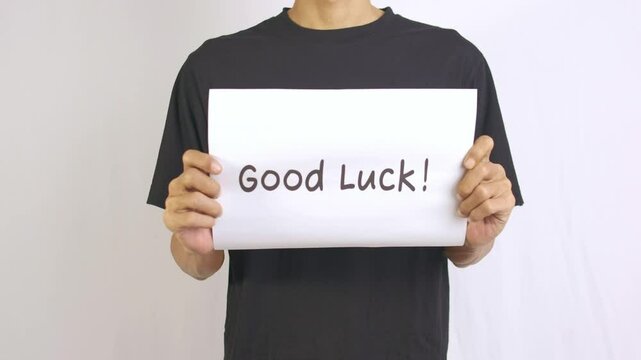 a footage of a man standing holding a paper that says good luck