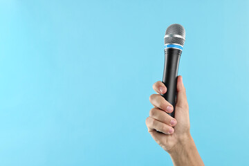 Man with microphone on light blue background, closeup. Space for text