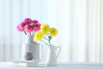 Beautiful flowers in vases and books on white wooden table at home. Space for text