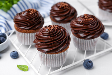 Tasty cupcakes with chocolate cream and blueberries on white tiled table, closeup