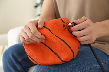 Man inflating basketball ball with air compressor indoors, closeup