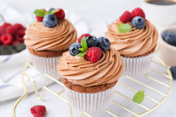 Tasty cupcakes with chocolate cream and berries on white table, closeup