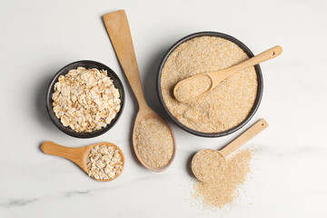 Oat bran and flakes on white marble table, flat lay
