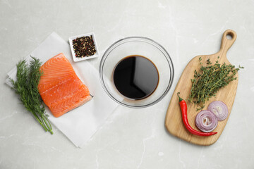Soy sauce in bowl, salmon fillet and spices on gray marble table, flat lay