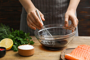 Woman making soy marinade for salmon fillet at wooden table, closeup