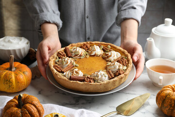 Woman with homemade pumpkin pie with whipped cream, seeds and cinnamon at white marble table, closeup