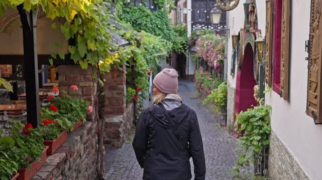Following a person walking down a colorful alleyway in the Rudesheim am Rhein town filled with small shops and wine vines, Germany