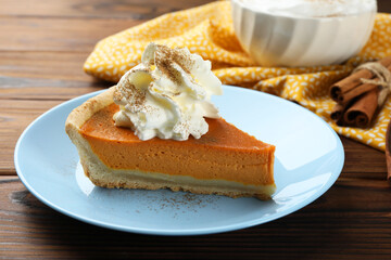 Piece of tasty homemade pumpkin pie with whipped cream on wooden table, closeup