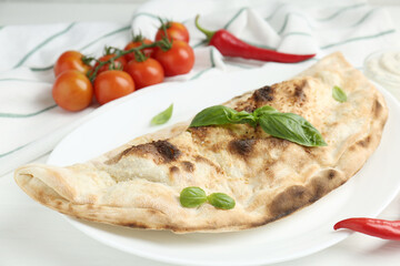 Tasty calzone, basil, chili pepper and tomatoes on white wooden table, closeup