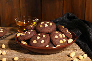 Tasty chocolate cookies with hazelnuts and tea on wooden table, closeup