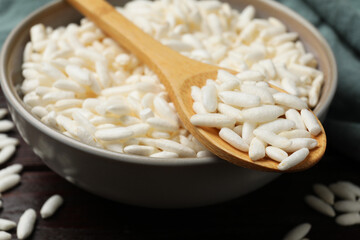 Puffed rice in bowl and spoon on wooden table, closeup