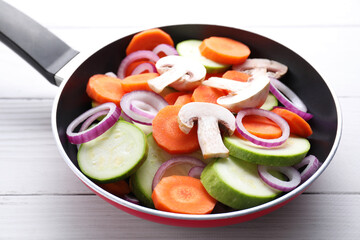 Frying pan with mix of fresh vegetables and mushrooms on white wooden table, closeup
