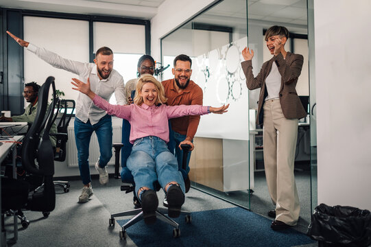 Business colleagues pushing businesswoman on office chair, having fun at work