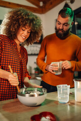 Couple preparing dough in kitchen, mixing ingredients in bowl