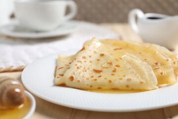 Tasty crepes with honey on wooden table, closeup