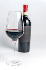 Glass of Red Wine with Bottle in Background on White.