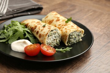 Tasty rolled crepes with cottage cheese and spinach served on wooden table, closeup