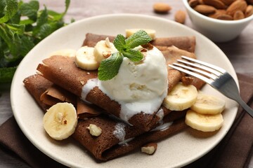 Delicious chocolate crepes with banana, nuts, mint and scoop of ice cream on table, closeup