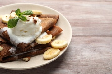 Delicious chocolate crepes with banana, walnuts, mint and scoop of ice cream on wooden table, closeup. Space for text
