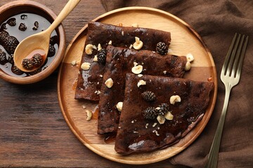 Delicious chocolate crepes with pine cone jam and nuts on wooden table, flat lay