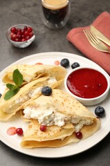 Delicious crepes with cottage cheese, jam, redcurrants and blueberries served on grey table, closeup