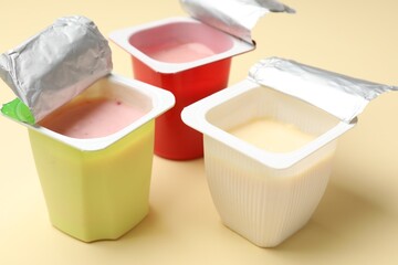 Delicious yogurts in plastic cups on beige background, closeup
