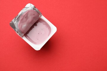 Delicious yogurt in plastic cup on red background, top view. Space for text
