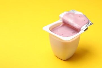 Delicious yogurt in plastic cup on yellow background, closeup. Space for text