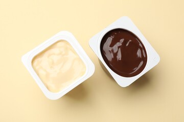 Delicious yogurts in plastic cups on yellow background, flat lay