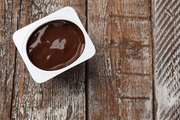 Delicious chocolate yogurt in plastic cup on wooden table, top view. Space for text
