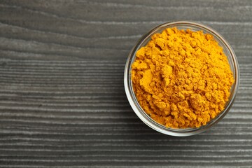 Turmeric powder in glass bowl on grey wooden table, top view. Space for text