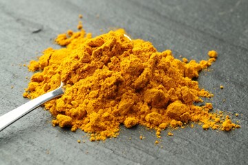 Turmeric powder and spoon on grey table, closeup