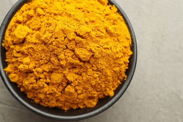 Turmeric powder in bowl on grey table, closeup. Top view