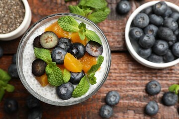 Delicious chia pudding with blueberries, peaches and mint in glass on wooden table, flat lay