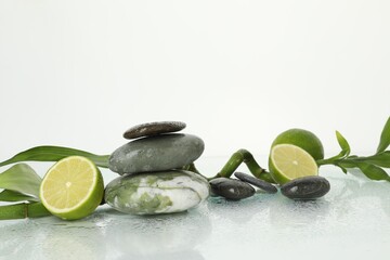 Spa composition with limes, massage stones and bamboo stem on wet surface against white background