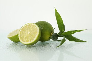 Fresh limes and bamboo leaves on wet surface against white background