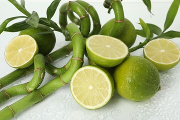 Fresh limes and bamboo stems on wet surface, closeup