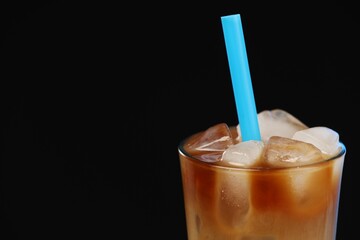 Refreshing iced coffee with milk in glass on black background, closeup. Space for text