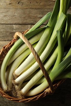 Fresh leeks in wicker basket on wooden table, top view