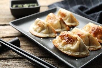 Delicious fried gyoza dumplings with sesame seeds served on wooden table, closeup