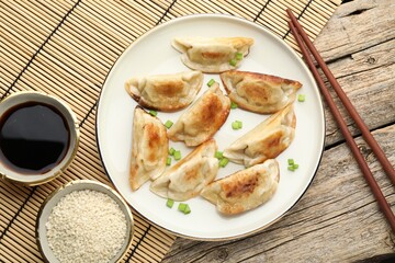 Delicious fried gyoza dumplings with green onions served on wooden table, flat lay