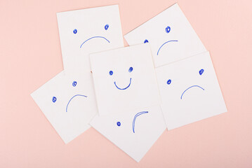 Smiley face among sad faces on paper cards on pink background.