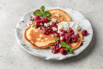 Homemade pancakes with yoghurt, berries and raspberry jam. Maslenitsa or Pancake day breakfast on gray background