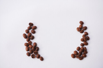 A collection of roasted coffee beans is symmetrically arranged on a white background, forming a mirrored pattern with an empty space in the center, highlighting their dark brown color and texture.