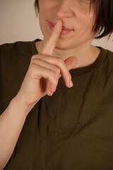 Close-up beauty portrait of woman showing silence sign and looking at camera.